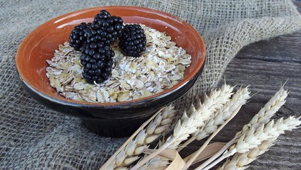 Flakes of five cereals in a Cup and fresh blackberries on a wooden background.