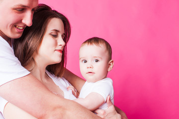 Beautiful family is posing with their infant, pink background