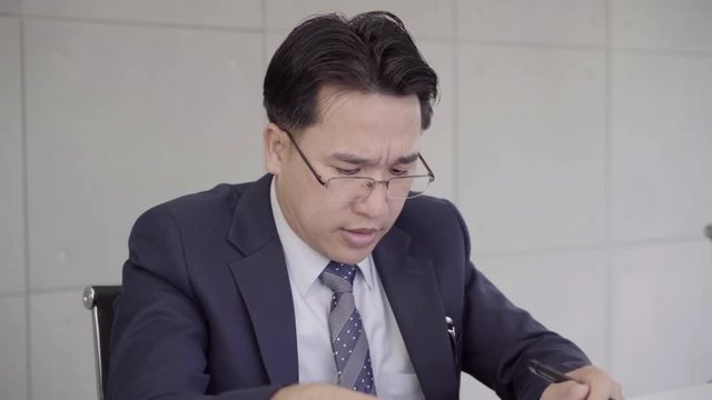 Slow motion - Businessman upset at desk in office. Asian businessman being depressed by working in office. Yong business man to think and not Work with stress Pretending to put his hand to the head.
