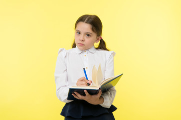 Girl cute schoolgirl in uniform hold book with information yellow background. Pupil get information from book. Child wear school uniform prepare for lesson information. Noticing information