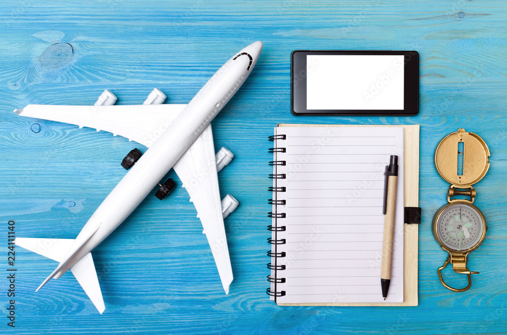 Wall mural toy airplane, blank page notepad, navigation compass and blank screen mobile phone on blue table bac