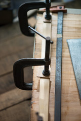 Woodworking. Wood working project on work bench in a dim workshop. Clamped pieces of wood with c-clamps and bar clamp. Shot in low key and shallow depth of field. Focus is on forehand clamp pad.