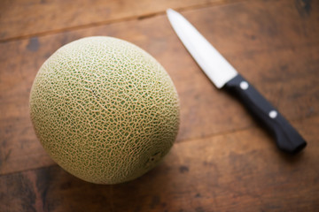 Melon on a rustic kitchen table, with knife in background. Intentionally shot with extremely shallow depth of field.