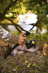 A fisherman with a fishing rod. Close-up of a hand holding a spinning rod and twisting a coil. Colorful view, blurred background, selective focus.
