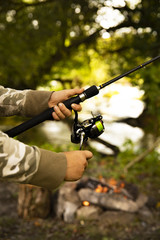 Fototapeta premium A fisherman with a fishing rod. Close-up of a hand holding a spinning rod and twisting a coil. Colorful view, blurred background, selective focus.