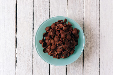 Plate of chocolate cereals on white wooden background