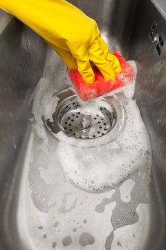 a gloved hand washes the sink with a sponge