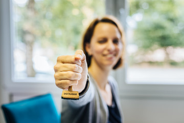 Eine Frau in einem Büro hält einen Stempel aus Holz mit dem Wort 