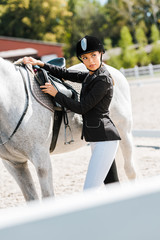 beautiful female equestrian fixing horse saddle at horse club