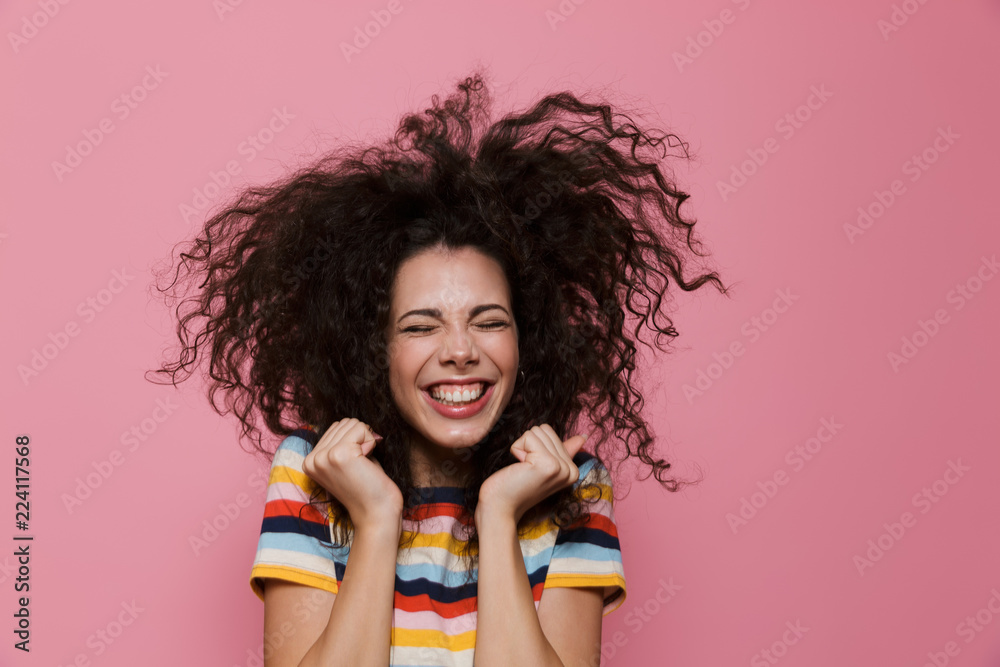 Wall mural Image of joyous woman 20s with curly hair rejoicing and smiling, isolated over pink background