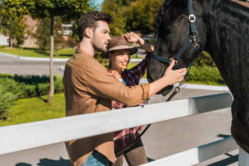 female and male equestrians palming black horse at ranch