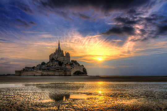 Beautiful view of historic landmark Le Mont Saint-Michel in Normandy, France, a famous UNESCO world heritage site and tourist attraction, at sunset with reflection