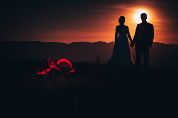 Man and woman silhouette in sunset light. Red poppy flowers in front of photo. Valentine or wedding...
