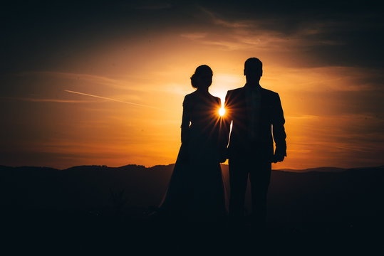 Man and woman silhouette, wedding couple. Orange sun ray between them