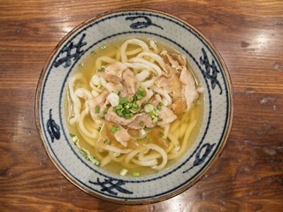 Ramen or Japanese noodles topping with Chashu or boiling pork, onions and scallions in clear soup served in a bowl on brown wooden table