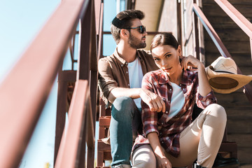 cowboy and cowgirl in casual clothes sitting on staircase at ranch