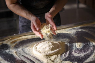 Baker sprinkles dough for pizza by semolina