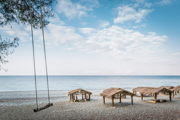 Beach canopies with a reed roof on the shore of a calm sea and swing for the entertainment of tourists