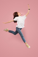 Always on mobile. Full length of pretty young woman taking phone and making selfie while jumping against pink studio background. Mobile, motion, movement, business concepts