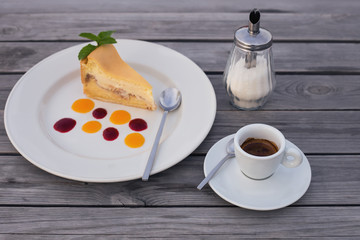  a cup of coffee and piece of appetizing cheesecake with drops of jam on a plate  on a wooden background