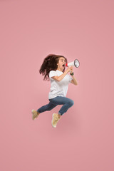 Beautiful young woman jumping with megaphone isolated over pink background. Runnin girl in motion...