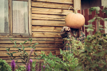Person wear pumpkin on head. Standing near wooden house and points a finger at the camera. Scarry concept of hallowen