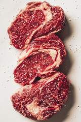 Obraz premium top view of three pieces of raw meat steaks and salt on white surface