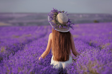 Beautiful healthy long hair. Back view of Young teen girl in hat over lavender field. Happy carefree woman with shiny hairstyle enjoying sunset. Outdoors portrait. Provence, France.