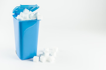 Blue trash can full of sugar cubes, white background