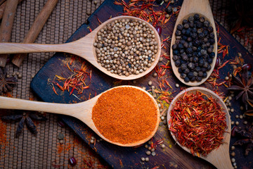 Colorful various spice and herbs in wood spoon on natural texture burned wood plate.