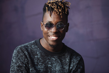 Stylish smile african american man rapper with dreadlocks at violet wall background