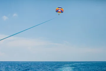 Fotobehang Mensen vliegen aan een kleurrijke parachute getrokken door een motorboot © meatbull