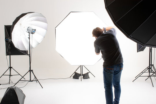 Photographer  working in modern lighting studio with many kinds of flash and accessories. taking to empty area in look like shot to someone. Idea for adding people or object to photo