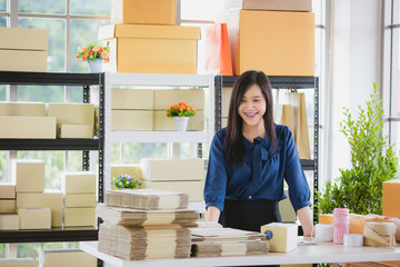 Young and beautiful Asian woman standing among several boxes and checking parcels, working in the house office. Concept for home base business and startup ownership
