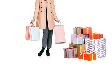 cropped shot of woman holding shopping bags and standing near gift boxes isolated on white