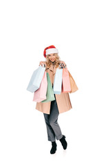 beautiful happy young woman in santa hat holding shopping bags and smiling at camera isolated on white