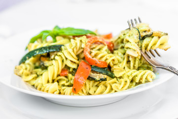 Italian food - pasta with zucchini and pepper and pesto sauce on a white plate close-up