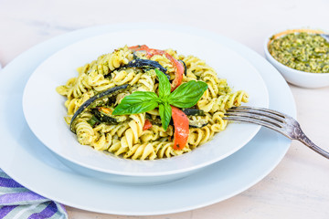 Italian vegetarian traditional dish - fusilli pasta with zucchini and pepper and pesto sauce on a white plate close-up
