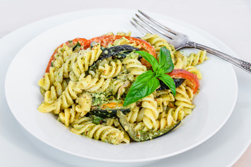Italian vegetarian traditional dish - fusilli pasta with zucchini and pepper and pesto sauce on a white plate close-up