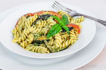 Italian vegetarian traditional dish - fusilli pasta with zucchini and pepper and pesto sauce on a white plate close-up