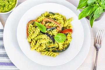 Italian vegetarian food - fusilli pasta with zucchini and pepper and pesto sauce on a white plate close-up, top view