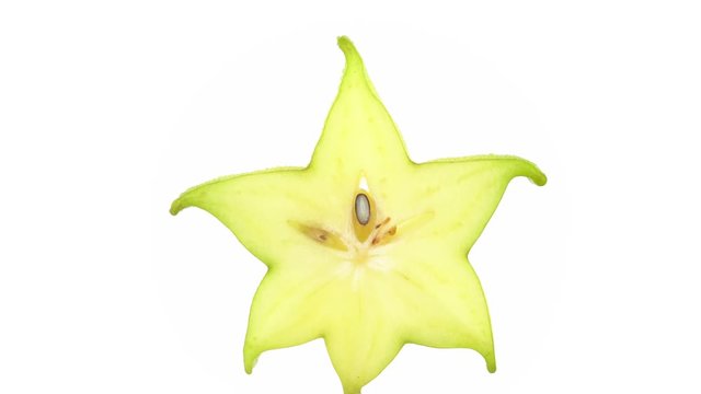 One star shaped slice of ripe carambola fruit with water drops. Slowly rotating on the turntable isolated on the white background. Close up. Macro.