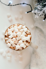 Hot cocoa with marshmallow, cinnamon, warm cozy light plaid, Christmas tree branches and a garland on white table. Top view.