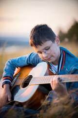 Young teen boy playing acoustic guitar at summer field