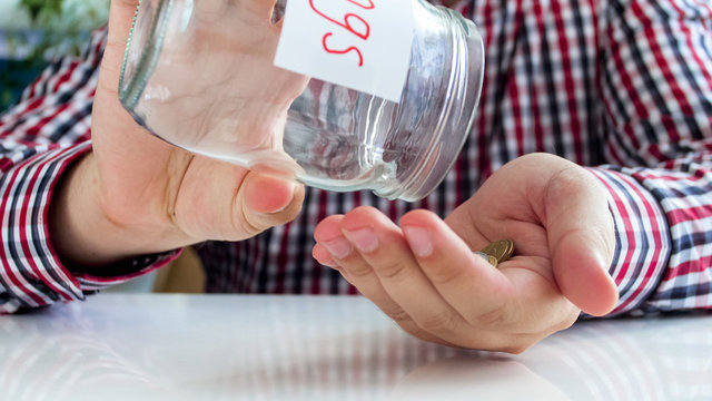 Closeup image of young man pouring few coins on hands for glass jar with money savings