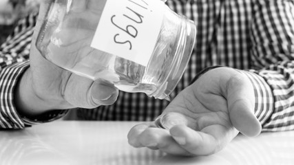 Black and white image of young man emptying glass jar with money savings