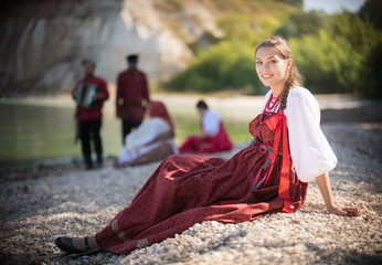 A beautiful girl in red Russian national costume pose for the camera on the background of an amazing landscape
