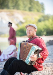 A man in Russian national costume stand on the background of an amazing landscape playing accordion