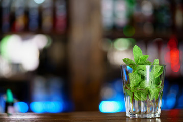 leaves of fresh mint are in a glass for preparation of a drink on the table on the background of the interior of the cafe. Close-up