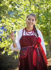Smiling young woman in russian folk costume on the foliage background
